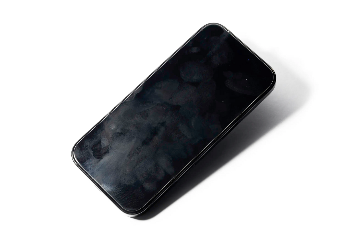 A smartphone with a smudged, reflective screen is shown on a white surface, angled slightly to the side.